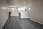 Located at 3625 Banbury Dr in Riverside, California, this single-story unit showcases a clean, modern aesthetic throughout its well-designed layout. Light gray wood-style flooring runs continuously across the living spaces, complementing the warm beige walls and white trim for a cohesive, neutral palette.

The open living area is anchored by soaring vaulted ceilings and a ceiling fan, with a pass-through connection to the kitchen that enhances the sense of openness. A sliding door leads to an outdoor patio area, allowing natural light to fill the space. A secondary room features dual windows overlooking mature trees, offering a bright and pleasant atmosphere.

The galley-style kitchen is well-appointed with crisp white shaker cabinetry, white quartz countertops, stainless steel appliances including a dishwasher, range, and refrigerator, and a deep stainless sink. The layout maximizes storage and counter space efficiently.

Bedrooms feature mirrored sliding closet doors and continued light flooring, while the bathroom is finished with white shaker cabinetry, quartz countertops, a framed mirror, brushed nickel hardware, and wood-style tile flooring. The textured ceilings add subtle architectural character throughout the home.