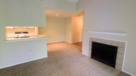 This single-floor residential space offers a thoughtfully arranged layout that balances comfort and functionality. The living area serves as the heart of the home, highlighted by a classic tiled fireplace with a clean white mantle — an inviting focal point that adds warmth and character to the room. Soft, neutral-toned carpeting extends throughout the main living space, contributing to a cozy and comfortable atmosphere.

An open pass-through counter connects the kitchen to the living area, promoting a sense of openness and making the space feel interconnected. The kitchen benefits from recessed lighting, providing bright and even illumination. Smooth, light-toned walls in a soft sage hue lend a calm and airy quality to the interior.

The entryway, visible from the living area, features hard flooring that transitions into the carpeted main space, offering a practical and welcoming arrival point. Recessed lighting in the ceiling adds to the well-lit ambiance without imposing on the clean lines of the interior. Overall, the space presents a neutral, move-in-ready environment with classic design elements that provide a comfortable and livable setting.