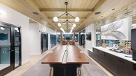 Located at 100 Chestnut St in Ashland, Massachusetts, this generously sized single-floor amenity space delivers a sophisticated, modern aesthetic across a thoughtfully designed layout. The entrance leads into an open, light-filled interior where warm wood-paneled ceilings, herringbone-patterned flooring, and globe pendant light fixtures set an elevated tone. A striking live-edge communal table anchors the main gathering area, complemented by sleek dark cabinetry and mirrored tile backsplash accents. Glass-paneled doors connect to private meeting rooms and a conference space, offering functional flexibility. The lounge area features soft seating, colorful accent chairs, and column-lined open space beneath a multi-pendant chandelier, creating an inviting social environment. A dedicated dining area showcases bold geometric diamond-patterned tile flooring, dark-topped communal tables, and pendant lighting, framed by teal accent walls adorned with curated artwork. The game room includes a full billiards table, built-in counter seating, a wall-mounted television, and statement art pieces beneath a brass pendant light. Throughout the space, teal walls, warm wood tones, and carefully selected furnishings create a cohesive, contemporary ambiance designed to encourage community and productivity.