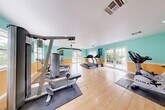Located at 6700 Nova Dr in Davie, Florida, this fitness center offers a bright and energetic environment designed to support a well-rounded workout routine. The space is characterized by a lively two-tone color scheme — aqua teal on the upper walls and warm orange on the lower — creating a vibrant, motivating atmosphere that sets it apart from a typical gym setting.

Light hardwood flooring spans the entire space, providing a clean and polished foundation for the variety of equipment arranged throughout. Rubber exercise mats are positioned beneath the strength machines, adding both safety and functionality. The fitness center is equipped with multiple cable and weight machines, treadmills, a stationary bike, and additional cardio equipment, offering a comprehensive range of workout options.

Natural light flows generously into the room through multiple windows and two sets of elegant French doors, which open directly to a lush outdoor area. This connection to the outdoors enhances the airy, open feel of the space. Recessed lighting in the white ceiling ensures the room remains well-lit at all times. Colorful artwork adorns the walls, adding a creative touch to the functional environment. The overall ambiance is welcoming, energetic, and well-suited for daily fitness use.