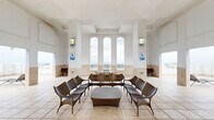 Located at 225 Evernia St in the heart of West Palm Beach, this generously sized rooftop space offers a seamless blend of indoor and outdoor living with stunning panoramic views of the Intracoastal Waterway, marina, and the downtown skyline. The space is finished throughout in neutral travertine-style floor tiles that extend from the covered interior lounges to the open-air terrace, creating a cohesive and polished aesthetic.

The two interior living areas feature soaring ceilings with elegant arched detailing, warm wall sconces, and floor-to-ceiling arched windows that frame sweeping water and city views on all sides. One lounge area is appointed with wicker and rattan seating arranged around a central coffee table, ideal for social gatherings. The other showcases a more open layout with high coffered ceilings and direct access to the terrace.

The expansive outdoor terrace wraps around the building and is dotted with striking oversized royal blue cylindrical planters hosting towering royal palm trees, lending a resort-like tropical atmosphere. Lounge chairs are positioned throughout to take full advantage of the breathtaking water views. Decorative medallion accents adorn the soft blue exterior walls, adding refined architectural character to this elevated outdoor retreat.