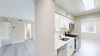 This single-floor residence offers a clean, modern aesthetic throughout, characterized by a neutral warm-gray color palette, white trim, and a combination of light luxury vinyl plank flooring and plush carpeting. The galley-style kitchen is a standout feature, outfitted with crisp white shaker cabinetry, quartz countertops, a stainless steel undermount sink, and a full suite of stainless steel appliances including a gas range, over-the-range microwave, dishwasher, and refrigerator. A louvered pantry door provides additional storage. The open living area is generously sized, featuring light plank flooring and a sliding glass door that opens to a private balcony, filling the space with natural light and outdoor views. Bedrooms are carpeted for comfort and feature windows with horizontal blinds that bring in natural light. Multiple bedrooms include closets, with at least one featuring a reach-in closet. A central hallway connects the living spaces to the bedrooms and bathroom, which includes tiled walls. Throughout the residence, clean lines, consistent finishes, and an abundance of natural light create a bright, functional, and comfortable living environment.