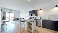 Located at 5005 Old Cedar Lake Rd in St. Louis Park, MN, this well-appointed one-bedroom unit offers a thoughtfully designed open-concept layout with modern finishes throughout. Light wood-look flooring runs through the main living areas, complementing the clean, contemporary aesthetic.

The kitchen is a standout feature, showcasing sleek dark navy cabinetry, stainless steel appliances including a range, dishwasher, and refrigerator, and a striking geometric-patterned tile backsplash. A central kitchen island with bar seating provides additional prep space and casual dining.

The kitchen flows seamlessly into the living area, where a sliding glass door opens to a private balcony, bringing in abundant natural light and outdoor views of the surrounding St. Louis Park neighborhood. The living space offers a comfortable and versatile layout ideal for both relaxing and entertaining.

The bedroom is a calm, neutral retreat featuring plush carpeting, crisp white walls, and a large black-framed window that frames sky views and fills the room with daylight. An adjacent area provides closet and storage space with built-in shelving. The unit is completed by a dedicated laundry area, adding everyday convenience to this efficiently designed and modern urban residence.