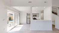 Located at 10826 W Florence Dr in Boise, Idaho, this two-story home presents a clean, modern aesthetic defined by a crisp white palette and light-toned finishes. The main level showcases an open-concept layout where the living area flows seamlessly into the kitchen. Large sliding glass doors invite abundant natural light, creating a bright and airy atmosphere throughout. Light wood-look flooring anchors the main living spaces, while a white peninsula counter serves as a natural divider between the kitchen and living area. The kitchen is outfitted with gray shaker-style cabinetry and a full suite of stainless steel appliances, including a refrigerator, range, and microwave. A staircase with wood treads and black iron balusters connects the main floor to the upper level, adding a refined architectural detail to the interior. The upper floor features carpeted bedrooms that offer a comfortable, quiet retreat, each with access to natural light through windows with blinds. Bathrooms are finished with light wood-look flooring, white vanities, and grab bars, combining practicality with a tidy, contemporary design. Throughout both floors, the home maintains a cohesive, neutral aesthetic that is both functional and inviting.