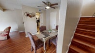 This two-story residence offers a well-organized layout across both levels, combining comfortable living spaces with practical design throughout. The living room serves as the focal point of the main floor, boasting soaring vaulted ceilings that lend a sense of openness and volume. Rich hardwood flooring runs underfoot, while a classically framed fireplace anchors one wall, adding warmth and character to the space. Large windows dressed with sheer curtains allow natural light to filter softly into the room. Adjacent to the living room, the dining area features hardwood flooring, a ceiling fan overhead, and a full wall of mirrors that enhance the sense of depth. It connects directly to the kitchen, which is outfitted with white cabinetry, granite-style countertops, tile flooring, and stainless steel appliances including a range and dishwasher. A louvered door adds a classic touch to the kitchen entry. Upstairs, the primary bedroom offers plush carpeting, a ceiling fan, and direct access to an ensuite bathroom. The bathroom is finished with neutral tile surround in the tub-shower combination, accented by a decorative mosaic tile border, providing a clean and polished look. Throughout the home, a warm, neutral color palette creates a cohesive and inviting ambiance.