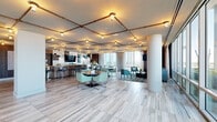 Located at 1762 Tysons Central Street in Vienna, VA, this sophisticated amenity lounge spans a generously sized single floor, offering a thoughtfully designed communal space ideal for socializing, working, and entertaining. The interior is defined by its striking copper pipe grid ceiling system, which frames warm Edison-style lighting throughout and lends an industrial-chic aesthetic to the overall design.

Light wood-look tile flooring runs seamlessly across the entire floor plate, complementing the cool teal, slate, and warm wood tones found in the furnishings and millwork. Floor-to-ceiling glass windows and doors wrap the perimeter of the space, flooding the interior with abundant natural light and providing sweeping panoramic views of the Tysons skyline and surrounding landscape. Doors lead directly to an outdoor terrace, extending the usable space further.

The lounge is organized into distinct functional zones. A full-service kitchen and bar area features sleek gray cabinetry, butcher block and stone countertops, a large island with bar seating, draft taps, and a bold tiled backsplash accented by industrial pendant lighting. Adjacent dining and lounge areas offer a variety of seating arrangements, from intimate round tables to plush sofas and lounge chairs. A dedicated entertainment corner includes a flat-screen TV and a pool table, rounding out this well-appointed communal retreat.