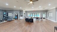 Located at 501 NC-54 W in Carrboro, NC, this single-floor commercial space offers a generously sized, well-appointed environment designed for both productivity and comfort. The open-plan main area features warm hardwood-style flooring, recessed lighting, and large glass entry doors that flood the space with natural light and provide views of the surrounding greenery. Multiple workstations are arranged throughout the open floor, complemented by a ceiling fan and textured ceilings that add a residential warmth to the professional setting.

The living room lounge area serves as a standout feature, anchored by a dramatic full-height brick fireplace wall with a mounted flat-screen television. Comfortable seating, a coffee table, and a lush green wall panel create an inviting, relaxed atmosphere ideal for meetings or breaks.

The fully equipped kitchen is thoughtfully designed with white shaker cabinetry, a subway tile backsplash, dark countertops, and stainless steel appliances including a refrigerator, range, and microwave. A breakfast bar with pendant lighting and bar stools provides additional seating. Windows throughout the kitchen offer pleasant outdoor views, enhancing the bright and airy feel of the entire space.