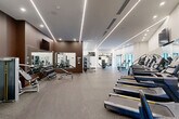 Located at 800 Monroe St SW in Huntsville, Alabama, this generously sized fitness center offers a comprehensive exercise facility designed with both function and aesthetics in mind. The space features a contemporary interior characterized by crisp white walls accented with rich brown feature walls, durable rubber-flooring, and a sleek ceiling lined with recessed and linear LED lighting that creates a bright, energizing atmosphere throughout.

The cardio zone is well-appointed with a row of modern treadmills, elliptical machines, and stationary bikes, providing ample space for users to exercise comfortably. A dedicated strength training area includes a full dumbbell rack, multiple weight benches, cable machines, and multi-functional training stations from leading equipment brands such as Matrix. Floor-to-ceiling mirrors along the walls amplify the sense of openness and allow users to monitor their form during workouts.

Wall-mounted flat-screen televisions provide entertainment during cardio sessions. Large floor-to-ceiling windows and glass doors along one wall flood the space with natural light and offer views of an outdoor pool area, seamlessly connecting the interior fitness environment with the exterior amenities. The overall design is polished and professionally appointed, making it a well-equipped destination for a complete workout experience.