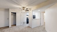 This single-floor residence at 1808 Visscher Dr in Elkhart, Indiana, offers a straightforward, functional layout with well-defined living spaces throughout. The open floor plan connects the main living area to the kitchen via a pass-through counter, promoting a sense of openness and ease of movement. The living room is generously proportioned, featuring plush carpeting, a ceiling fan with light fixture, and a sliding glass door fitted with vertical blinds that allows natural light to flow in while providing direct outdoor access.

The kitchen is efficiently designed in a galley configuration, featuring white cabinetry with contemporary hardware, light granite-patterned countertops, light wood-style flooring, and black appliances including a refrigerator, gas range, and dishwasher. A decorative upper cabinet with lattice detailing adds a subtle design element.

The bedrooms are carpeted and equipped with ceiling fans. One bedroom includes an en-suite bathroom with a tub/shower combination and direct closet access, while another bedroom features a window with natural light and a dedicated closet. Additional storage is provided throughout the unit via multiple closets. The space maintains a neutral color palette with beige tones and white trim, creating a clean, move-in ready environment.