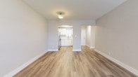 This single-floor unit offers a thoughtfully updated interior with a cohesive, modern aesthetic. Light wood-style flooring runs throughout, complementing the soft neutral walls and crisp white trim. The open living area is generously sized, with flush-mount lighting and a clear sightline into the kitchen, creating a connected, airy feel.

The kitchen is well-appointed with white flat-panel cabinetry, light-toned countertops, and stainless steel appliances including a refrigerator, electric range, and over-the-range microwave. A single-basin sink sits beneath a window fitted with blinds, allowing natural light into the space. Ample upper and lower cabinet storage adds to the kitchen's functionality.

A hallway connects the living area to the sleeping quarters, passing a louvered closet door and a bathroom. The bathroom features a soaking tub with white mosaic tile surround and a window above for natural ventilation. The bedroom is a comfortable size, with a dedicated closet, a window with blinds, and a textured ceiling. Overall, the unit presents a clean, move-in-ready environment with modern updates throughout.