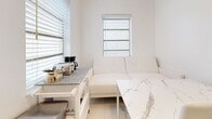 Located at 545 Michigan Ave in the heart of Miami Beach, FL, this single-floor studio unit offers a clean, minimalist aesthetic defined by a crisp all-white palette and polished marble-look flooring that runs seamlessly throughout the entire space. Natural light filters in through multiple windows fitted with horizontal blinds, lending the interior a bright and airy ambiance.

The main living and sleeping area is thoughtfully arranged, featuring a comfortable bed with a neutral upholstered headboard, a compact sofa, and a small desk and chair — providing distinct zones for rest, relaxation, and work within a single open room. A ceiling fan and flush-mount lighting provide both comfort and illumination.

The kitchen is fully equipped with white shaker-style cabinetry, a stainless steel sink, a full-size refrigerator, an electric range, and classic white subway tile backsplash — offering all essential cooking amenities in a compact, efficient layout.

The bathroom continues the marble-inspired design with large-format white marble-look wall tiles lining the tub-shower combination, which features a sliding glass door enclosure. A ribbed white vanity and wall-mounted fixtures complete the polished look.

This studio presents a cohesive, modern design that is well-suited for those seeking a clean and functional living space in one of Miami Beach's most accessible neighborhoods.