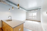 Located at 101 Virginia St in downtown Sioux City, Iowa, this one-bedroom, one-bathroom unit offers a thoughtfully designed open-concept layout that seamlessly combines the living room, dining area, and kitchen into a single, bright space. The kitchen is well-appointed with light maple cabinetry, a subway tile backsplash, stainless steel appliances including a refrigerator with ice maker, electric range, and microwave, complemented by a peninsula with a double stainless steel sink and neutral countertops — ideal for both cooking and casual dining. A striking industrial aesthetic is carried throughout, with exposed silver ductwork running across the ceilings, adding a modern urban character. Large windows in the living area and bedroom invite generous natural light and offer views of the surrounding cityscape. The carpeted bedroom provides a comfortable retreat with its own closet access. The clean, white bathroom features a full tub-shower combo and wood-look flooring. A dedicated in-unit laundry room houses a full-size washer and dryer. Wood-look flooring flows through the main living areas, while two closets offer ample storage throughout this efficiently organized home.