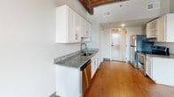 Located at 12 S 17th St in Richmond, VA, this single-floor unit offers a compelling blend of historic character and contemporary updates. The open living area is an immediate standout, showcasing exposed original brick walls, rich hardwood flooring, and a striking wood-plank ceiling supported by heavy timber beams — elements that speak to the building's storied past. Tall ceilings amplify the sense of openness, while multiple windows allow natural light to filter in, highlighting the warmth of the natural materials throughout.

The kitchen features white shaker-style cabinetry, granite countertops, a stainless steel sink, and stainless steel appliances, offering a clean, modern contrast to the rustic surroundings. The layout flows efficiently toward the entry door, which is finished with warm wood tones.

The bathroom is thoughtfully updated with a walk-in shower, a white vanity topped with granite, and a backlit LED mirror that provides both functional and ambient lighting. Tile flooring completes the clean, contemporary aesthetic.

An additional room with carpeted flooring and an electrical panel serves as a flexible utility or storage space, featuring an exposed timber post that carries the building's historic industrial character throughout. This space is ideal for those who appreciate the authenticity of Richmond's architectural heritage paired with modern conveniences.