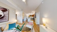 This single-floor residence is designed with a contemporary open-concept layout that connects the living, dining, and kitchen areas into one cohesive space. Light wood-look flooring flows throughout, complementing the neutral-toned walls and tall ceilings that lend a sense of airiness. The kitchen is a standout feature, equipped with stainless steel appliances including a range, microwave, and French door refrigerator. Two-tone cabinetry pairs warm wood upper cabinets with sage green lower cabinets, accented by white quartz countertops and a subway tile backsplash. A central island with pendant lighting provides additional workspace and seating. The living area is generously proportioned and opens to a balcony through large windows that bring in abundant natural light and outdoor views. The bedrooms are well-sized with tall ceilings and large windows. The primary bedroom includes a walk-in closet and direct access to an en-suite bathroom featuring a glass-enclosed shower, wood vanity, and white quartz countertop. A second bathroom offers a full tub-shower combination with hexagonal tile flooring. The overall ambiance is clean, modern, and welcoming.