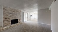 This single-story residence offers a thoughtfully organized layout across a comfortable footprint, accommodating two bedrooms, one bathroom, a combined kitchen and living room, a hallway, and two closets. The living room serves as the focal point of the home, defined by a full-height brick accent wall housing a wood-burning fireplace with a raised brick hearth. Built-in shelving flanks the fireplace, adding functional display space. Plush wall-to-wall carpeting extends throughout the living area, and a sliding glass door provides access to the outdoors. A textured popcorn ceiling and neutral gray walls complete the room's character.

The kitchen features white cabinetry, granite-look countertops, a stainless steel sink with a matte black faucet, and stainless steel appliances including a refrigerator, range, and dishwasher. Wood-look tile flooring adds a clean, durable finish to this space.

Both bedrooms are carpeted and equipped with ceiling fans. The primary bedroom includes natural light from a window with blinds. The bathroom offers a wide granite-top vanity with white cabinetry, a matte black faucet, a large mirror with modern lighting, and a tub-shower combination, all finished with wood-look tile flooring.