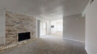 This single-story residence offers a thoughtfully organized layout across a comfortable footprint, accommodating two bedrooms, one bathroom, a combined kitchen and living room, a hallway, and two closets. The living room serves as the focal point of the home, defined by a full-height brick accent wall housing a wood-burning fireplace with a raised brick hearth. Built-in shelving flanks the fireplace, adding functional display space. Plush wall-to-wall carpeting extends throughout the living area, and a sliding glass door provides access to the outdoors. A textured popcorn ceiling and neutral gray walls complete the room's character.

The kitchen features white cabinetry, granite-look countertops, a stainless steel sink with a matte black faucet, and stainless steel appliances including a refrigerator, range, and dishwasher. Wood-look tile flooring adds a clean, durable finish to this space.

Both bedrooms are carpeted and equipped with ceiling fans. The primary bedroom includes natural light from a window with blinds. The bathroom offers a wide granite-top vanity with white cabinetry, a matte black faucet, a large mirror with modern lighting, and a tub-shower combination, all finished with wood-look tile flooring.