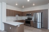 Located at 713 N Main St in Meridian, Idaho, this single-level 2-bedroom, 2-bathroom unit offers a clean, contemporary design with consistent light wood flooring flowing throughout. The open-concept kitchen is well-appointed with flat-front wood-toned cabinetry, white quartz countertops, a marble-style tile backsplash, and a full suite of stainless steel appliances including a French door refrigerator, range, microwave, and dishwasher. A peninsula provides additional counter space and casual seating, while a wall-mounted mini-split unit offers climate control. The living area is bright and airy, benefiting from natural light and an open layout. Both bedrooms feature large windows with views of the surrounding Meridian streetscape, flooding the rooms with natural light. Each bedroom includes a sliding barn-style closet door for a modern touch. The two bathrooms are finished consistently with wood-toned vanities, white quartz countertops, large mirrors, and light fixtures overhead. One bathroom features a soaking tub with tiled surround, while the second offers a walk-in shower. A dedicated closet provides additional storage. The overall aesthetic is modern and minimalist, with neutral tones creating a cohesive and versatile living environment.