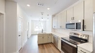 Located at 1735 N Greenville Ave in Richardson, TX, this one-bedroom, one-bathroom unit offers a thoughtfully designed layout that maximizes every square foot of its compact footprint. The open-concept floor plan seamlessly connects the kitchen and living area, creating a sense of spaciousness despite the intimate scale.

The kitchen is a standout feature, outfitted with stainless steel appliances including a GE electric range, over-the-range microwave, side-by-side refrigerator with ice maker, and dishwasher. Two-toned cabinetry — with crisp white upper cabinets and warm greige lowers — pairs with white subway tile backsplash and light countertops for a clean, modern aesthetic. A peninsula with an undermount sink adds prep space and visual flow into the main living area.

Warm wood-look flooring runs continuously throughout the unit, complementing the bright, neutral color palette. The living area benefits from a ceiling fan and a large window dressed with blinds, allowing ample natural light while maintaining privacy. The bedroom features its own window overlooking the exterior, enhancing the airy feel.

The bathroom includes a full soaking tub with a shower, framed by floor-to-ceiling neutral tile, offering a clean and functional retreat. Six-panel doors with matte black hardware add a contemporary touch throughout the unit.