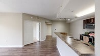 Located in Orlando's Falcon Parc community, this 2-bedroom, 1-bathroom residence offers a well-designed single-floor layout with a neutral color palette and warm-toned finishes throughout. The open-concept living, dining, and kitchen area forms the heart of the home, featuring rich dark wood-style flooring, track lighting, and a ceiling fan. The kitchen is outfitted with dark espresso cabinetry, granite-style countertops, stainless steel appliances including a range, microwave, and refrigerator, plus a pantry for additional storage. A peninsula with a sink connects the kitchen to the living area, enhancing the open flow. The living room opens directly onto a private balcony through sliding glass doors, filling the space with natural light and offering outdoor views of landscaped grounds. Both bedrooms feature plush carpeting and ceiling fans, with the primary bedroom providing a generous, comfortable retreat. The bathroom includes a wide vanity with dark cabinetry, granite-style countertops, and a large mirror with overhead lighting. Tile flooring completes the bathroom. Additional highlights include three closets, a dedicated laundry area with a stacked washer and dryer unit, and a utility room, ensuring practical convenience throughout.