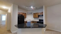 Located at 8439 Dorchester Rd in North Charleston, South Carolina, this single-floor space offers a well-appointed layout designed for everyday comfort and functionality. The kitchen serves as a central highlight, showcasing dark granite countertops with a breakfast bar overhang that provides a casual dining or workspace area. Warm-toned wood cabinetry lines the walls, offering generous storage, while black appliances — including a full-size refrigerator and a gas range — lend a sleek, cohesive aesthetic. A stainless steel sink is positioned beneath upper cabinetry, and a ventilation hood is centrally mounted above the cooking area. Track lighting illuminates the kitchen efficiently, enhancing the overall brightness of the space. The open-facing design of the kitchen toward the adjoining living area creates a connected, airy feel throughout the floor plan. Neutral wall tones and light-colored flooring in the adjacent areas complement the kitchen's darker finishes, creating a balanced and inviting interior atmosphere. This single-story layout offers accessibility and ease of movement throughout, making it a practical and comfortable living environment in the heart of North Charleston.