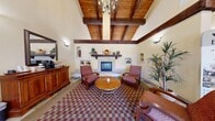 Located at 1975 Maxwell Ave in Woodland, California, this single-story community clubhouse offers a generously sized, amenity-rich layout designed for both socializing and relaxation. The grand entrance hallway greets visitors with soaring vaulted ceilings, elegant chandelier lighting, and a striking multicolored stone tile floor that sets a welcoming, upscale tone throughout. Large glass entry doors invite abundant natural light, while plantation shutters on adjacent windows provide adjustable privacy.

The great room serves as the heart of the space, featuring dramatic exposed wood beam ceilings with warm tongue-and-groove paneling, a central stone fireplace with a decorative wood mantel, and built-in arched wall niches that add architectural character. Comfortable seating and a patterned area rug complete the inviting atmosphere.

The game room is well-appointed with a full-size billiard table as its centerpiece, accented by a Tiffany-style pendant light, recessed lighting, framed artwork, and shuttered windows. The media room offers a cozy retreat with a large flat-screen television and comfortable sectional seating. An accessible shower facility with grab bars, a fold-down bench, and hand-held fixtures ensures the space accommodates all users. Throughout, the design reflects a consistent Spanish-inspired aesthetic with warm tones and quality finishes.