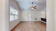 This single-story home presents a well-organized layout with a clean, contemporary aesthetic throughout. The spacious living area immediately draws attention with its vaulted ceiling and ceiling fan, creating an airy, open atmosphere. Warm hardwood-style flooring runs through the main living spaces, complementing the neutral white walls and natural light streaming in through large windows with blinds.

The kitchen is a functional highlight, featuring rich dark cabinetry that extends to the ceiling for ample storage, granite countertops, and stainless steel appliances including a range and French door refrigerator. A substantial kitchen island with a built-in sink provides additional prep space and casual seating potential, all illuminated by recessed lighting.

Bedroom spaces offer plush carpeted flooring, ceiling fans, and multiple windows that fill the rooms with natural light. The bathrooms are finished with tile flooring, granite-topped dark vanities, and clean white fixtures, including a soaking tub in the full bath and a private water closet.

Completing the home is a generously sized attached two-car garage equipped with an automatic opener, featuring a concrete floor and ample room for storage alongside vehicles.