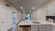 This well-appointed single-floor residence offers a thoughtfully designed open-concept layout that seamlessly connects the kitchen and living areas. The kitchen is a standout feature, showcasing granite countertops with a peninsula that doubles as a breakfast bar, gray shaker-style cabinetry, a bold black tile backsplash, and a full suite of stainless steel appliances including a refrigerator, electric range, over-the-range microwave, and dishwasher. A stainless steel sink with a modern gooseneck faucet completes the space. Wood-style plank flooring runs throughout the main living areas, adding warmth and durability, while recessed lighting provides a clean, contemporary ambiance. The living area opens to a private balcony through a sliding glass door, allowing natural light to fill the space. The bedroom features plush carpeting and a window fitted with blinds for privacy and light control. The bathroom is finished with a granite-topped vanity, gray cabinetry, wood-style tile flooring, and a tub-shower combination. Additional highlights include multiple interior doors with panel detailing, a walk-in closet, and a smart thermostat. The neutral color palette throughout creates a cohesive and inviting environment.
