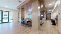 This thoughtfully designed single-floor amenity space seamlessly blends contemporary and industrial aesthetics to create an inviting, multi-functional environment. Throughout the space, striking geometric-patterned hardwood flooring anchors each zone and ties the layout together cohesively.

The open entry area features light wood paneling, a warm wood-clad ceiling, and built-in millwork columns that define distinct gathering spaces without fully enclosing them. A central lounge zone is furnished with leather and upholstered seating, framed by sheer-curtained windows that allow abundant natural light to filter through.

A prominent bar area showcases a long white countertop set atop bold navy-blue cabinetry, complemented by tufted upholstered bar stools and a marble-look backsplash with open industrial-style shelving. A second, more intimate bar features blue fluted tile, warm wood ceilings, and leather counter stools, adding a sophisticated contrast.

Exposed brick walls punctuate the space with raw, textural character, while a corridor lined with brick leads to additional rooms, including a catering-style kitchen with gray cabinetry, white countertops, and open shelving. A relaxed seating nook with soft lounge chairs is positioned near floor-to-ceiling curtained windows. Pendant lighting clusters and wall sconces throughout add curated, modern illumination, completing the space's refined yet welcoming atmosphere.