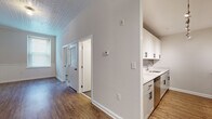 This single-floor space blends classic architectural details with modern updates, creating a bright and functional living environment. The galley-style kitchen is a standout feature, outfitted with crisp white shaker cabinets accented by matte black hardware, quartz countertops, an undermount sink, and a full suite of stainless steel appliances including a refrigerator, range, microwave, and dishwasher. Track lighting overhead ensures the space is well-lit and practical.

Throughout the unit, warm hardwood-style flooring adds a welcoming, cohesive feel, while the decorative tin ceilings lend a distinctive, period-inspired character to the space. Tall ceilings in the main hallway and common areas enhance the sense of openness, allowing natural light from windows to filter through generously.

The living areas feature neutral gray-toned walls, clean white baseboards, and crown molding details that contribute to a polished, finished aesthetic. The layout, as seen in the dollhouse view, is well-organized with clearly defined zones for living, sleeping, and utility areas.

The bathroom is finished with large-format gray tile flooring, a full soaking tub and shower combo with classic white subway tile surround, chrome fixtures, and a white vanity, offering a clean and timeless design. Overall, the space presents a thoughtfully renovated interior with a consistent modern-classic aesthetic.