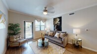 This well-designed single-floor residence showcases a cohesive blend of modern style and everyday comfort across its thoughtfully arranged spaces. The living room serves as the heart of the home, featuring warm hardwood-style flooring, crown molding, and a ceiling fan overhead. Natural light pours in through large windows dressed with elegant valances, while a sliding glass door opens to a private balcony, extending the living space outdoors. A bold statement artwork anchors the room, adding a sophisticated artistic touch.

Adjacent to the living area, the dining space offers an intimate setting highlighted by a rich wood dining table and a striking multi-panel gold abstract art arrangement on the wall. A convenient closet nearby provides additional storage.

The kitchen is both functional and stylish, outfitted with dark espresso cabinetry, granite countertops, and black appliances including a refrigerator, range, and built-in microwave. Hardwood-style flooring continues throughout, tying the spaces together seamlessly.

The bedroom is a serene retreat featuring plush carpeting, multiple windows that invite natural light and outdoor views, and a ceiling fan for year-round comfort. The bathroom is finished with dark wood cabinetry, granite countertops, a large vanity mirror, and light tile flooring, offering a clean and refined aesthetic.