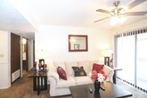 This single-floor residence offers a well-organized layout with distinct living, sleeping, dining, and kitchen areas. The living room serves as the central gathering space, featuring wall-to-wall carpeting, a ceiling fan with integrated lighting, and a sliding glass door fitted with vertical blinds that provides access to an outdoor area and brings in natural light. A wall-mounted mirror and framed artwork add character to the room.

The galley-style kitchen is efficiently arranged, featuring dark wood cabinetry, laminate countertops, a double-basin sink, and white appliances including a refrigerator, electric range, and dishwasher. Tile flooring runs throughout the kitchen. Adjacent to the kitchen, the dining area provides additional functional space.

The unit includes two bedrooms, both finished with soft carpeting and windows fitted with horizontal blinds. The primary bedroom features a walk-in closet, while a second carpeted bedroom offers a bright, versatile space. Two bathrooms serve the unit, each with tile flooring, vanity cabinetry, and a tub-shower combination. Textured ceilings are consistent throughout, contributing to the cohesive, practical character of the space.