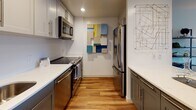Located at 11 Broad Canal Way in Cambridge's vibrant Kendall Square neighborhood, this single-floor residence offers a thoughtfully designed layout with contemporary finishes throughout. The open-plan living and dining area is anchored by warm hardwood flooring, crisp white walls, and large windows that frame impressive views of the Cambridge and Boston skyline. The living space comfortably accommodates both a seating area and a dining nook, with open shelving providing additional display and storage options.

The galley-style kitchen is outfitted with grey shaker cabinetry, white countertops, and a full suite of stainless steel appliances, including a range, microwave, and refrigerator. Recessed lighting enhances the clean, modern aesthetic.

The bedroom is a standout space, benefiting from a large picture window with sweeping city and waterway views. Neutral carpet, soft natural light, and ample room make it a comfortable retreat. The adjacent bathroom features hardwood-style flooring, a tub-shower combination, and a vanity with updated fixtures. The overall ambiance of the residence is modern and bright, with a cohesive design sensibility that blends functionality with urban sophistication.