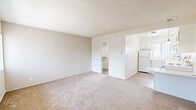 Located at 7923 Reseda Blvd in Reseda, CA, this efficiently designed single-floor unit offers a practical layout comprising a living room, kitchen, bathroom, and closet. The living room features neutral carpet flooring and a textured ceiling, with a wall-mounted air conditioning unit providing climate control. A large window with vertical blinds allows natural light to brighten the space and offers views of the surrounding exterior. The transition from carpet to wood-look flooring marks the entry area near the front door. The kitchen is neatly arranged in an L-shaped configuration, outfitted with white cabinetry, tile countertops, a white refrigerator, and a white coil-burner range. A window above the sink brings in additional natural light, and a ceiling-mounted light fixture illuminates the space. The bathroom is clean and functional, featuring a white vanity with a single sink, a wood-framed mirror, a toilet, and a shower with a sliding glass door. A frosted window provides ventilation and privacy. The dedicated closet offers additional storage. Throughout the unit, a consistent light and neutral color palette creates a cohesive, bright ambiance well-suited for comfortable everyday living.