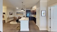 This single-floor residence offers a thoughtfully designed layout that balances comfort and functionality throughout. The open-concept kitchen is a standout feature, boasting rich dark-stained cabinetry, granite-style countertops, black appliances including a range and built-in microwave, and a large central island with pendant lighting overhead — seamlessly connecting to the dining area. The dining space is framed by crown molding and features hardwood-style flooring, creating an inviting atmosphere for gatherings. The living room continues the refined aesthetic with crown molding, a ceiling fan, and ample natural light filtering through windows dressed with stylish treatments, offering generous space for relaxing and entertaining. The bedrooms are carpeted for warmth and comfort, with one featuring a bold accent wall, a ceiling fan, and access to a spacious walk-in closet outfitted with wire shelving systems. The primary bedroom connects directly to a large walk-in closet and opens to the hallway. Two full bathrooms serve the residence: one features a combined tub and shower with a granite-topped vanity and wood-look flooring, while the second offers a clean, functional tub-shower combo. Throughout, neutral tones and consistent finishes create a cohesive and welcoming ambiance.