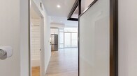 Located at 1810 State Street in San Diego's vibrant 92101 corridor, this contemporary unit on the seventh floor offers a thoughtfully designed single-level layout. Light wood-tone flooring runs throughout the entire space, creating a warm and cohesive aesthetic that complements the crisp white walls and recessed lighting overhead.

The open-concept kitchen is a standout feature, outfitted with white shaker cabinetry, dark countertops, a classic white subway tile backsplash, and a full suite of stainless steel appliances including a refrigerator, gas range, and microwave. Under-cabinet lighting adds both function and ambiance to the cooking space.

The main living area is bright and airy, benefiting from floor-to-ceiling sliding glass doors that flood the interior with natural light and provide access to an outdoor space. A mirrored sliding closet in the sleeping area enhances the sense of openness while maximizing storage.

The bathroom is cleanly appointed with a white vanity, framed mirror, pendant lighting, and a tiled tub-shower combination, maintaining the modern and minimal aesthetic found throughout the unit.

Dark-framed glass partition elements add an architectural detail that defines spaces without sacrificing the open feel. Overall, the unit presents a modern, move-in-ready environment with efficient use of its compact footprint.