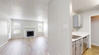 This thoughtfully designed single-floor residence offers a comfortable and functional layout across its one bedroom and one bathroom. The open-concept living room is a standout, featuring a classic wood-burning fireplace framed by a clean white surround, two windows that invite natural light, and durable wood-look plank flooring that extends throughout the main living areas. A ceiling fan adds to the room's practical comfort. The kitchen runs galley-style with gray cabinetry, white countertops, a stainless steel sink, and stainless appliances including a refrigerator and range. A curved breakfast bar provides casual seating and connects the kitchen to the living space. A pantry offers additional storage. The bedroom is generously sized, finished with soft carpet flooring, and includes access to a private outdoor area via a sliding glass door with vertical blinds. A dedicated closet adjoins the bedroom for organized storage. The full bathroom features wood-look tile flooring, a gray vanity with white countertop, a tub-shower combination, and brushed nickel hardware throughout. Textured ceilings are consistent across the space, contributing to a clean, neutral aesthetic throughout.