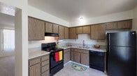 Located at 3701 Wible Rd in Bakersfield, California, this single-story unit offers a practical and straightforward layout designed for comfortable everyday living. The kitchen is a standout functional space, configured in an L-shape and equipped with a full suite of black appliances, including an electric range with overhead ventilation, a dishwasher, and a refrigerator. Warm-toned wood cabinetry lines both the upper and lower walls, providing generous storage, while light-speckled laminate countertops offer ample prep space. Tile-style flooring runs throughout the kitchen, contributing to easy maintenance.

The living areas and bedrooms feature neutral-toned carpet, lending a soft, comfortable feel underfoot. The rooms are finished with plain white walls and textured ceilings, creating a clean, move-in-ready aesthetic. A window fitted with vertical blinds in one of the rooms allows for natural light while maintaining privacy. A thermostat is visibly mounted in the living area, indicating centralized climate control.

The bathroom includes a tub and shower combination enclosed by sliding glass doors, tile-style flooring, and clean white walls with a textured finish. The overall layout, as visible from the floor plan, connects the main living space efficiently to the bedroom and bathroom areas, making this a well-organized, functional single-floor residence.