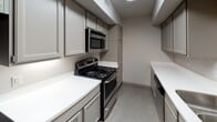 This single-floor unit offers a practical and comfortable layout with a cohesive design throughout. The galley-style kitchen is efficiently arranged with gray shaker cabinetry, crisp white countertops, and a full suite of stainless steel appliances including an electric range, over-the-range microwave, and dishwasher. Light-toned tile flooring and recessed ceiling lighting give the kitchen a clean, functional aesthetic.

The living area features warm, rich hardwood-style flooring that extends throughout the main living and bedroom spaces, creating a sense of continuity. Large windows allow natural light to filter in, brightening the open, neutral-toned walls. A textured ceiling adds subtle character to the space.

The bedroom offers a generous footprint with the same warm flooring, neutral walls, and a double-door closet providing ample storage. An additional room with a closet and hardwood-style floors can serve as a second bedroom, office, or flex space.

The bathroom includes a full soaking tub and shower combination with classic white tile surround, a toilet, a vanity with storage cabinet, and a mirror. The overall palette throughout the unit is neutral and clean, offering a versatile canvas that suits a variety of furnishing styles.