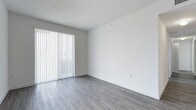 This single-floor space presents a fresh, minimalist aesthetic with a clean and functional design throughout. The main living area is immediately welcoming, featuring smooth grey laminate flooring that lends a contemporary feel underfoot. Crisp white walls provide a neutral, versatile backdrop that complements any style of furnishing or décor. A textured ceiling adds subtle character to the room overhead.

A prominent sliding glass door fitted with full-length vertical blinds serves as a key architectural feature, allowing natural light to filter softly into the space while also offering privacy and light control as needed. The door provides direct access to the outdoors, extending the sense of openness beyond the interior.

The layout is straightforward and efficient, making excellent use of the available footprint on its single level. The overall ambiance is bright and airy, enhanced by the light-toned flooring and white walls that work together to reflect available light and create a sense of spaciousness. The space is move-in ready, offering a clean slate well-suited for a variety of uses and personal styles. Its simple, uncluttered design allows occupants to easily envision and personalize the interior to their preferences.