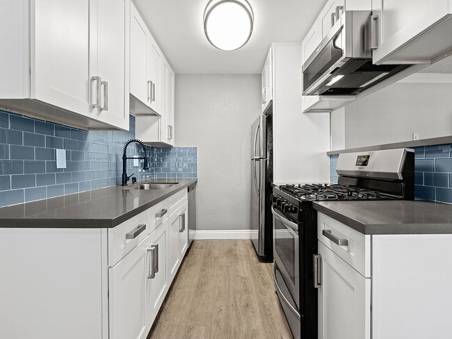 Blue tiled kitchen with stainless steel oven, microwave, and fridge. - National Apartments