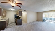 Located at 4410 Montebello Dr in Colorado Springs, CO, this single-floor, 2-bedroom, 1-bathroom unit offers a functional and comfortable layout. The open living room is generously sized, featuring neutral-toned carpet, a textured ceiling, and a ceiling fan with light fixture. A sliding glass door fitted with vertical blinds allows natural light to filter in and provides outdoor access. The living area flows seamlessly into the combined dining and kitchen space. The kitchen is well-appointed with warm wood-toned cabinetry, ample upper and lower cabinet storage, light countertops, a stainless steel sink, and black appliances including a refrigerator and electric range. Wood-style flooring adds a practical touch underfoot in this area. Both bedrooms are carpeted and finished with the same warm neutral tones, each featuring windows with blinds that bring in natural light. The primary bedroom is notably spacious and includes access to a closet, with a hallway connection to the shared full bathroom. Additional closet storage is distributed throughout the unit, and a hallway connects all main living areas efficiently. The textured ceilings are consistent throughout, contributing to a cohesive interior aesthetic.