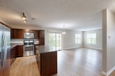 Located at 4817 N 133rd Plaza in Omaha, Nebraska, this single-floor, 2-bedroom, 2-bathroom home offers a thoughtfully designed layout with modern finishes throughout. The open-concept kitchen and living area serves as the heart of the home, featuring rich dark wood cabinetry, granite countertops, a central island, and a full suite of stainless steel appliances including a refrigerator, range, microwave, and dishwasher. Track lighting illuminates the kitchen, while a pendant light adds a decorative touch over the living space. Light wood-tone flooring flows throughout the main living areas, lending a clean and cohesive aesthetic. Sliding glass doors lead to a private balcony, allowing natural light to pour in and providing outdoor views. Both bedrooms are carpeted and generously sized, with windows that bring in additional natural light. The primary bedroom includes a ceiling fan and access to a walk-in closet outfitted with built-in shelving and hanging rods. The bathrooms feature granite-topped vanities with dark wood cabinetry and stylish framed mirrors. Neutral wall tones and textured ceilings complete the interior, creating a comfortable and functional living environment.