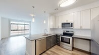 This well-appointed 2-bedroom, 2-bathroom residence features a thoughtfully designed single-level layout that maximizes functionality and style. The open-concept kitchen and living area serves as the heart of the home, showcasing a granite-topped peninsula island with an undermount sink and pendant lighting above. The kitchen is equipped with full stainless steel appliances, including a range, microwave, dishwasher, and refrigerator, complemented by two-tone cabinetry — crisp white upper cabinets paired with darker lower cabinets — set against a clean tile backsplash. Light wood-style flooring flows throughout the main living areas, while large floor-to-ceiling windows flood the living room with natural light and provide open exterior views. Both bedrooms are comfortably sized, with the primary bedroom offering generous square footage, soft carpet underfoot, and a window with outdoor views. Each bedroom includes its own dedicated closet for ample storage. The bathrooms are cleanly finished with tile flooring, white cabinetry, and a full tub-shower combination accented by a decorative mosaic tile border. Throughout the residence, a neutral white palette and modern fixtures create a bright, cohesive, and move-in-ready atmosphere.