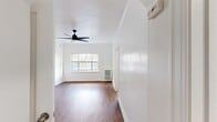 This single-floor unit offers an efficient and thoughtfully laid out living space, comprising a living room, kitchen, bathroom, closet, and hallway. Warm hardwood-style flooring runs throughout, providing a cohesive and inviting feel across all rooms.

The entry hallway leads naturally into the main living area, which is bright and airy thanks to a large window that lets in generous natural light. A sleek, modern ceiling fan with black blades serves as a functional focal point overhead. A decorative white fireplace surround adds a charming architectural detail to the living room, enhancing the overall character of the space.

The kitchen is well-appointed with white cabinetry, dark countertops, a black subway tile backsplash, a stainless steel sink, and a stainless steel refrigerator — offering a clean contrast of light and dark tones. A window in the kitchen provides additional natural light.

The bathroom is clean and minimal, featuring a full bathtub and a small window for ventilation. The spacious closet includes a hanging rod and multiple built-in shelving units, offering ample storage. Throughout the unit, crisp white walls and trim create a bright, neutral backdrop that makes the space feel open and versatile.