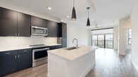 Located at 7557 Main St in Houston's vibrant Texas Medical Center corridor, this modern one-bedroom, two-bathroom residence offers a thoughtfully designed open-concept layout with contemporary finishes throughout. The combined kitchen and living area serves as the heart of the home, anchored by a sleek white quartz island with an undermount sink and pendant lighting overhead. Dark cabinetry provides striking contrast against a light tile backsplash, while a full suite of stainless steel appliances — including a French door refrigerator, range, built-in microwave, and dishwasher — completes the chef-friendly space. Wood-look flooring flows throughout, and floor-to-ceiling sliding glass doors in the living area open to a private balcony with open city views, allowing abundant natural light to fill the space. The bedroom is generously proportioned, featuring its own sliding glass door access to an outdoor balcony and a large walk-in closet with built-in shelving. The primary bathroom is spa-inspired, showcasing a dual-sink white quartz vanity with a wide frameless mirror and a glass-enclosed walk-in shower clad in large-format marble-style tile with hexagonal mosaic flooring. A dedicated in-unit laundry room houses a full-size side-by-side washer and dryer, adding everyday convenience to this polished Houston residence.