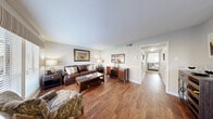 Located at 10580 Hammerly Blvd in Houston, TX, this single-floor residence offers a thoughtfully designed layout across two bedrooms and two bathrooms. The living room is a welcoming space featuring rich hardwood-style flooring, neutral walls, and a large window that allows natural light to fill the room. The adjacent dining area continues the same flooring and is highlighted by a pendant light fixture overhead, with a direct view into the kitchen. The galley-style kitchen is well-equipped with white cabinetry, marble-style countertops, a tile backsplash, and black appliances, opening conveniently into the dining space. The primary bedroom is generously sized, carpeted for comfort, and features a ceiling fan, a bright window, and a walk-in closet with multi-level shelving. The second bedroom is also carpeted, benefits from natural light through its window, and includes access to its own closet — making it suitable as a guest room or home office. Both bathrooms feature hardwood-style flooring, clean white fixtures, and marble-style countertops with updated vanities. A central hallway connects the bedrooms and bathrooms, contributing to the efficient and functional flow of the home.