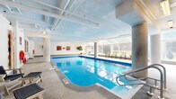 Located at 7307 Campeau Drive in Ottawa's K2T neighbourhood, this indoor aquatic facility offers a generously sized, single-floor space dedicated to swimming and relaxation. The centrepiece is a large rectangular indoor pool with clearly marked depth indicators, providing ample room for both lap swimming and leisure use. Stainless steel entry rails offer safe and convenient pool access.

The pool deck is finished with durable, slip-resistant terrazzo-style flooring and is lined with poolside lounge chairs, making it well-suited for both active use and unwinding. A row of large floor-to-ceiling windows along one side of the facility floods the space with natural light, offering views to the outdoors and creating an open, airy atmosphere despite the indoor setting. Concrete columns frame the pool area, adding to the functional architectural character of the space.

Supporting amenities are thoughtfully arranged around the pool perimeter, including change rooms, safety equipment such as life rings and posted health and safety regulations, and decorative potted plants that soften the utilitarian aesthetic. The exposed mechanical infrastructure on the ceiling contributes to the facility's practical design. The overall environment is clean, well-maintained, and functionally appointed, making it a comprehensive indoor aquatic amenity.