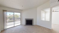 This single-floor space offers a clean, functional layout with a bright and open living area at its heart. The living room features plush, neutral-toned carpeting underfoot and crisp white walls that maximize the sense of light and space. A tile-surround fireplace serves as a natural focal point, adding warmth and character to the room. Sliding glass doors open directly to an outdoor patio, flooding the interior with natural light and providing easy access to the outdoors, where surrounding greenery and neighborhood views are visible. A pass-through window or architectural cutout on the adjacent wall adds a subtle design detail, enhancing the open feel and allowing light to flow between spaces. The textured ceiling adds a traditional touch consistent throughout the home. The overall ambiance is clean, airy, and move-in ready, with a neutral palette that provides a versatile backdrop for a variety of interior styles. This well-maintained space combines practical living features with comfortable, everyday functionality.