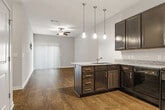 This 2-bedroom, 2-bathroom residence features a thoughtfully designed single-floor layout that maximizes comfort and functionality. The open-concept kitchen and living area serves as the heart of the home, anchored by a kitchen equipped with dark espresso cabinetry, granite countertops, a peninsula with an integrated sink, pendant lighting, and a full suite of black appliances including a refrigerator, range, microwave, and dishwasher. Wood-look flooring runs throughout the main living areas, complemented by a ceiling fan that enhances the airy feel of the living room. Both bedrooms offer plush wall-to-wall carpeting and neutral tones, creating a calm and restful atmosphere. The primary bedroom includes a dedicated walk-in closet outfitted with wire shelving for organized storage. The two bathrooms are finished with wood-look flooring, dark vanity cabinetry, and granite countertops. One bathroom features a shower enclosure, while the other offers a full tub-shower combination. A hallway connects the private areas of the residence, and clean white trim and neutral wall tones throughout the space contribute to a cohesive, modern aesthetic.