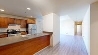 Located in Kansas City, MO, this 2-bedroom, 2-bathroom residence offers a practical and modern single-floor layout designed for comfortable urban living. The open-concept kitchen and living area serves as the heart of the home, anchored by a wraparound peninsula with a dark laminate countertop and warm wood-toned cabinetry. Stainless steel appliances — including a refrigerator and electric range — along with a double-basin sink and dishwasher complete the well-equipped kitchen. Light wood-style flooring runs throughout the common areas, lending a clean, cohesive look that flows seamlessly into the spacious living room, which benefits from recessed lighting and an open, airy feel. Both bedrooms feature soft carpeting and large windows dressed with blinds that frame views of the surrounding Kansas City skyline, filling the rooms with natural light. The primary bedroom is generously sized, offering ample space for furnishings. The two bathrooms are thoughtfully finished — one features a walk-in shower, warm wood vanity with ample drawer storage, and tile flooring, while the second includes a light-wood vanity with a large mirror. Throughout the residence, neutral tones and clean lines create a bright, move-in-ready environment well-suited to city living.